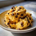Close-up of a scoop of thick, golden high protein cookie dough loaded with mini chocolate chips in a light bowl.