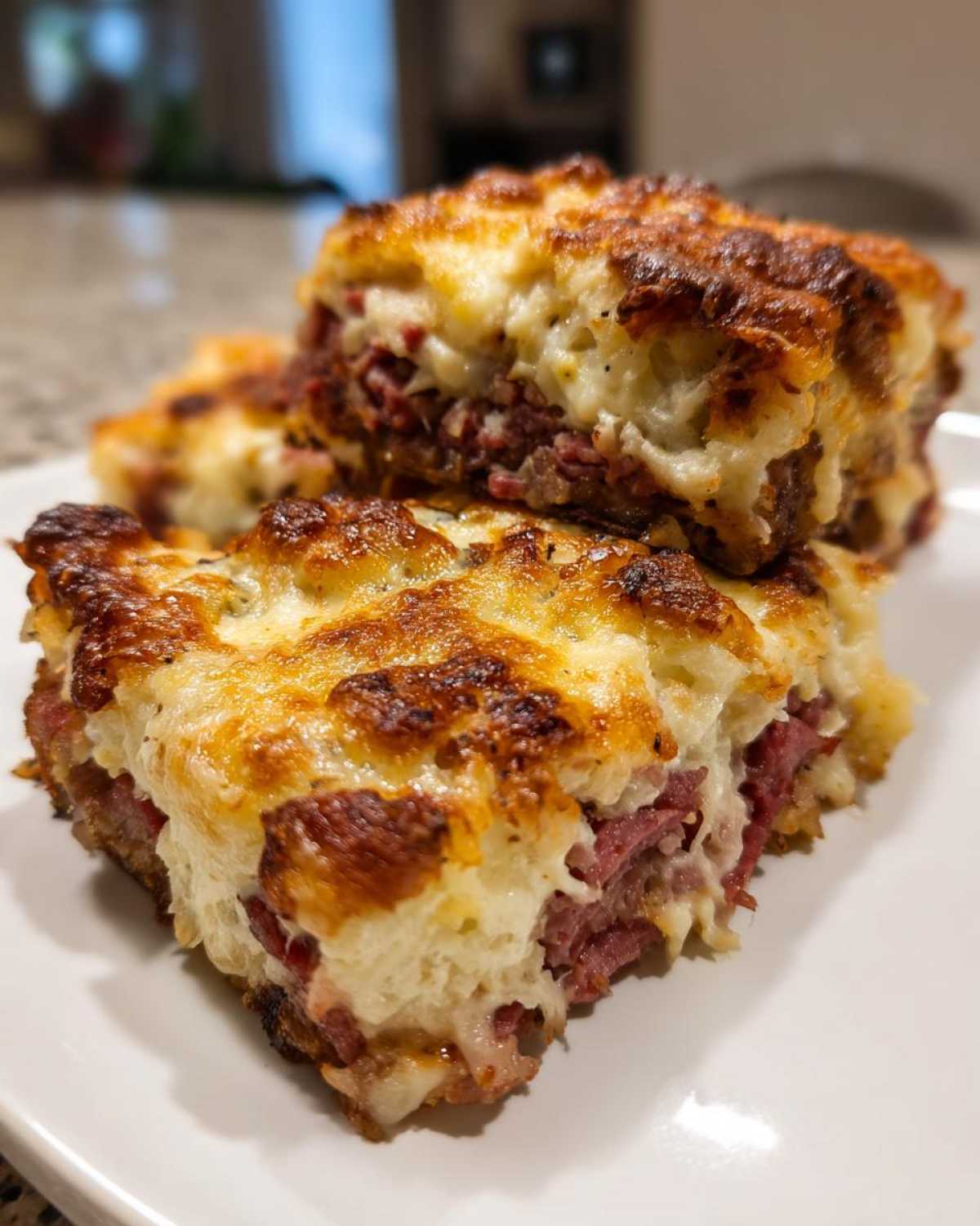 Two servings of a golden-brown, cheesy homemade reuben bake stacked on a white plate.