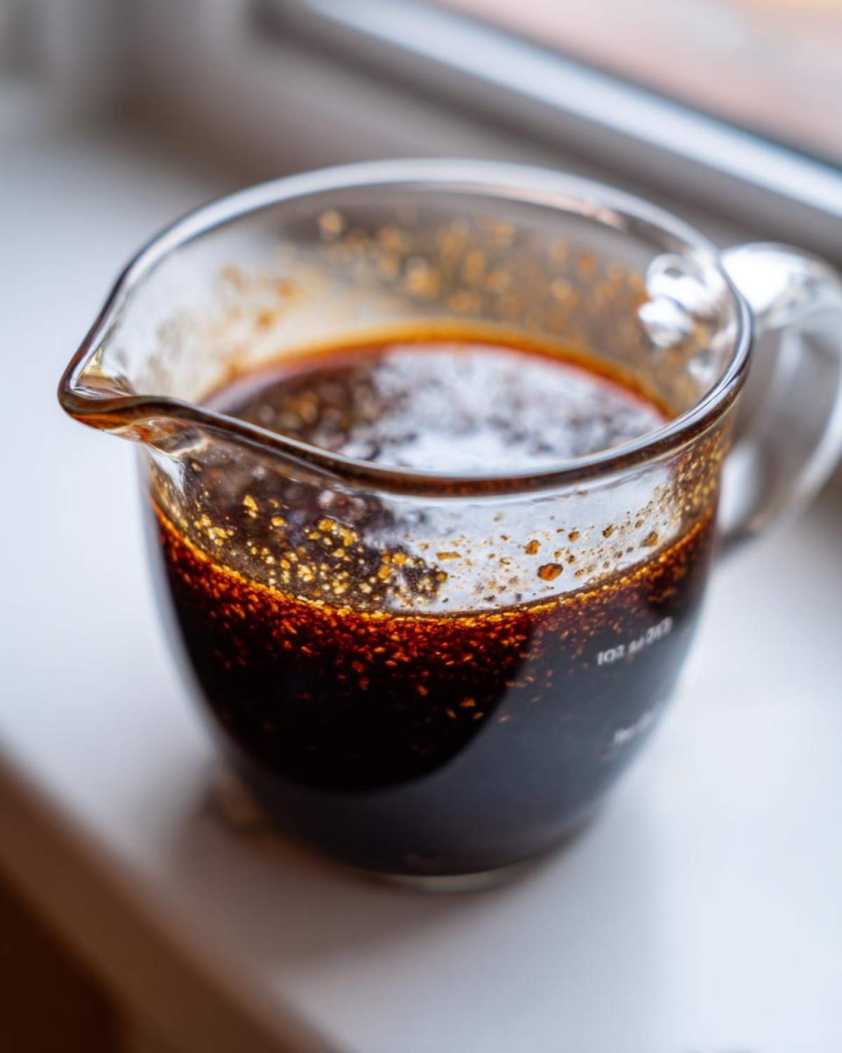 Close-up of rich, dark homemade teriyaki sauce resting in a clear glass measuring cup.