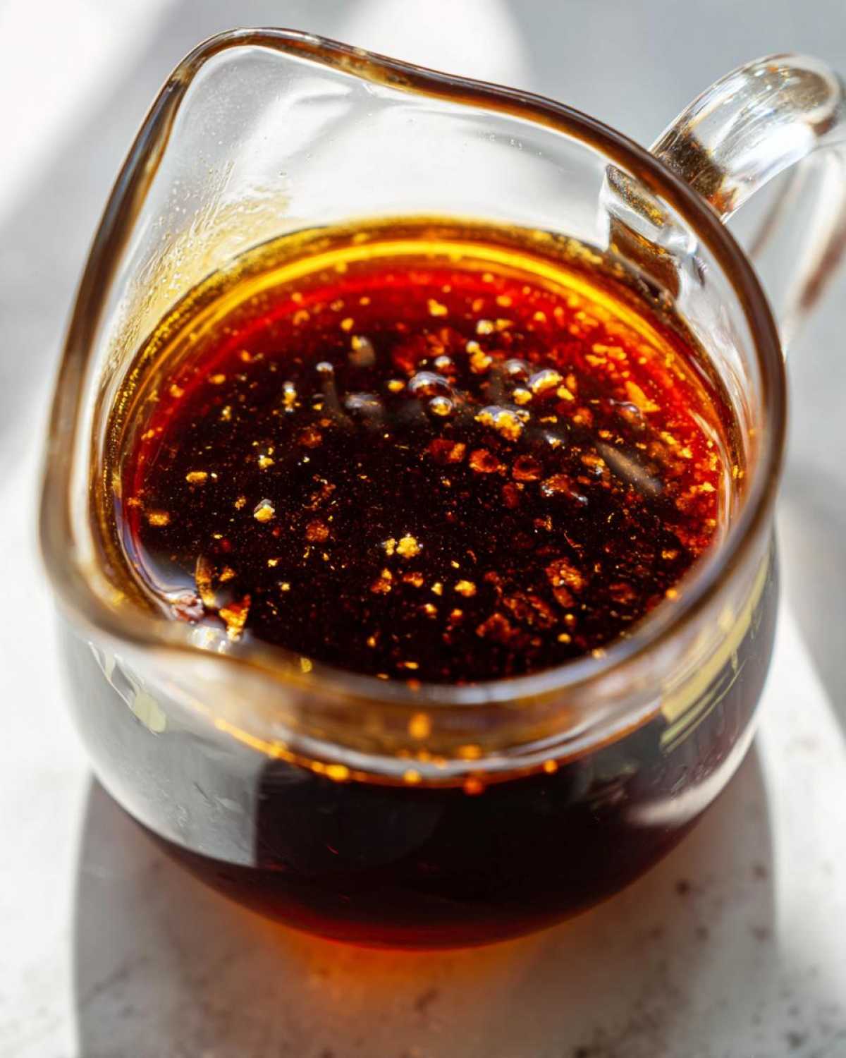 Close-up of rich, dark homemade teriyaki sauce with visible spice flecks in a small glass pitcher.