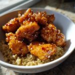 Close-up of Honey Garlic Chicken Quinoa, featuring glazed chicken pieces topped with sesame seeds over a bed of cooked quinoa in a white bowl.