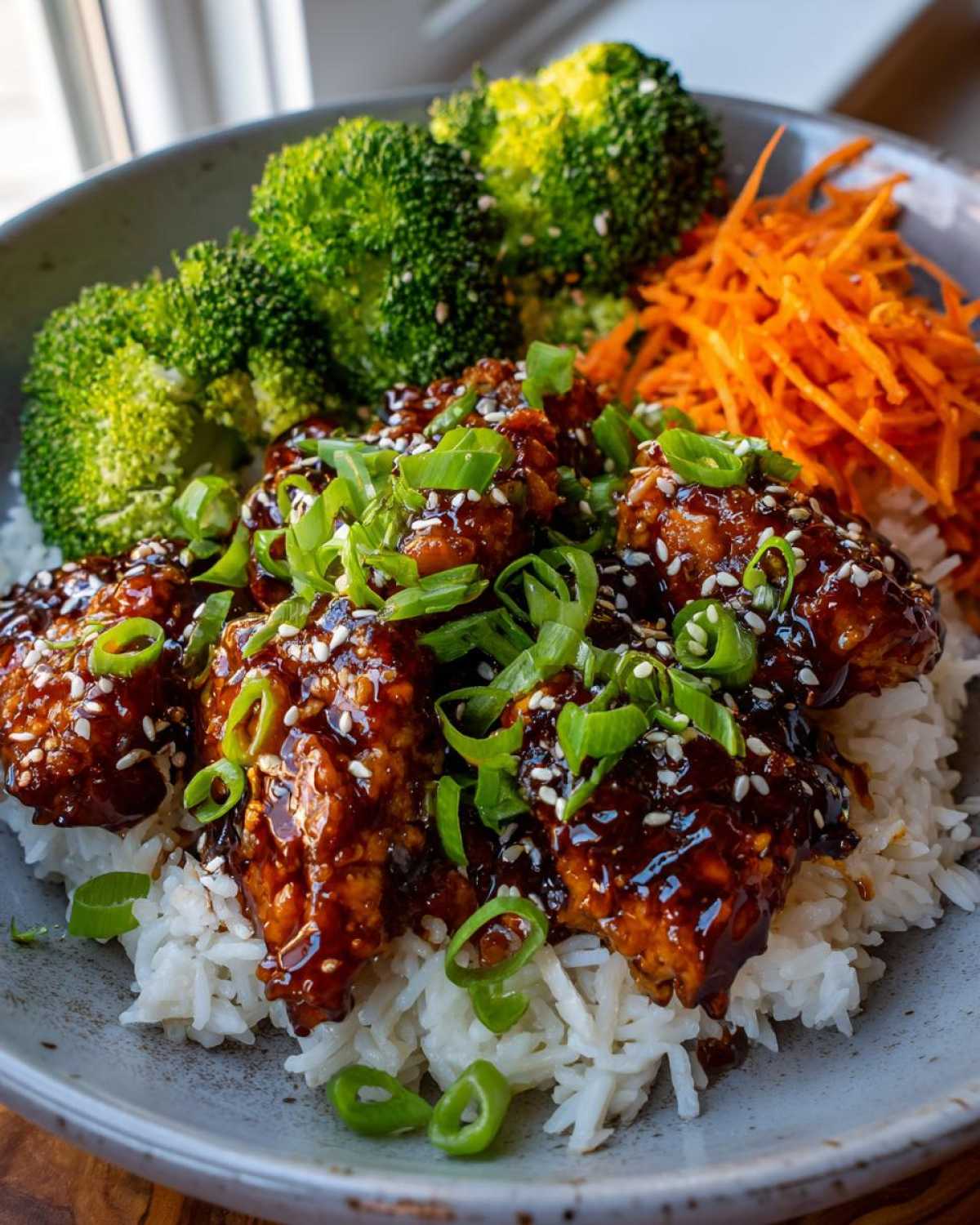 Close-up of a Honey Lime Chicken Rice Bowl featuring glazed chicken pieces over white rice with broccoli and shredded carrots.