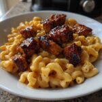 A white bowl filled with creamy macaroni and cheese topped with glazed pieces of Honey Pepper Chicken.
