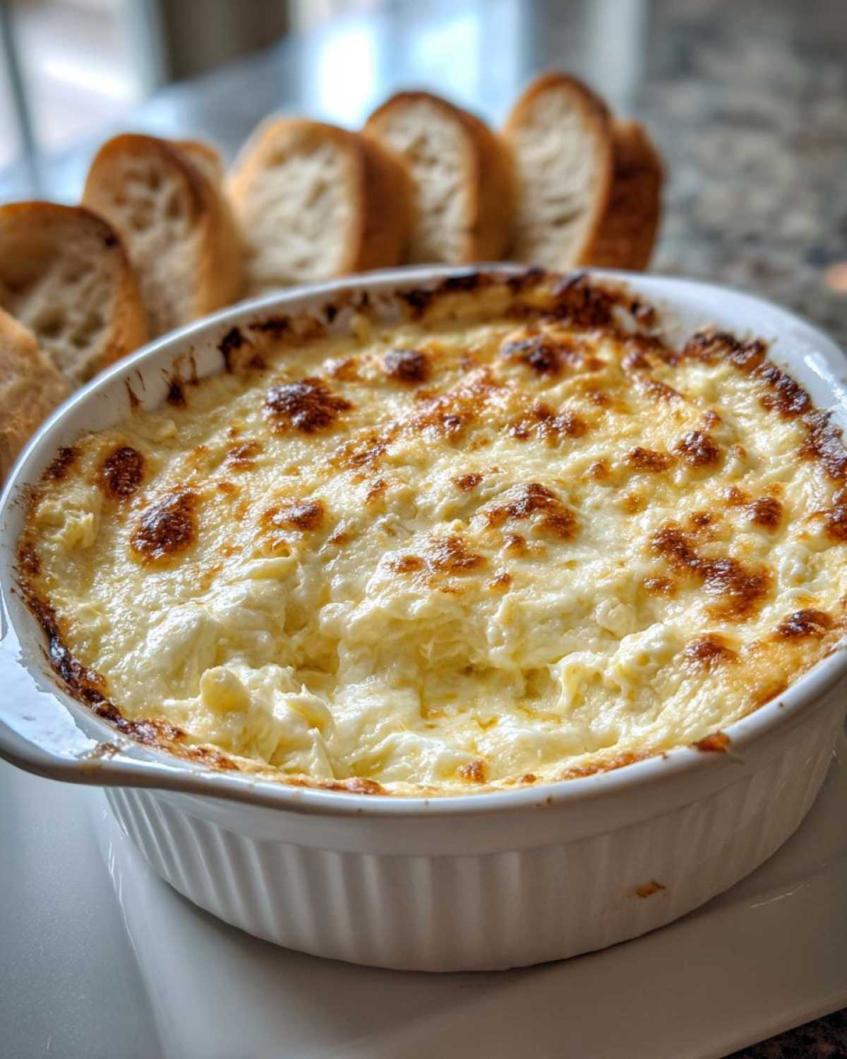 Close-up of a hot, cheesy bread dip baked in a white ramekin, served with sliced baguette pieces for dipping.