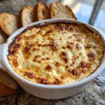 Close-up of a hot, cheesy bread dip with a golden-brown, bubbly crust, served with toasted bread slices.