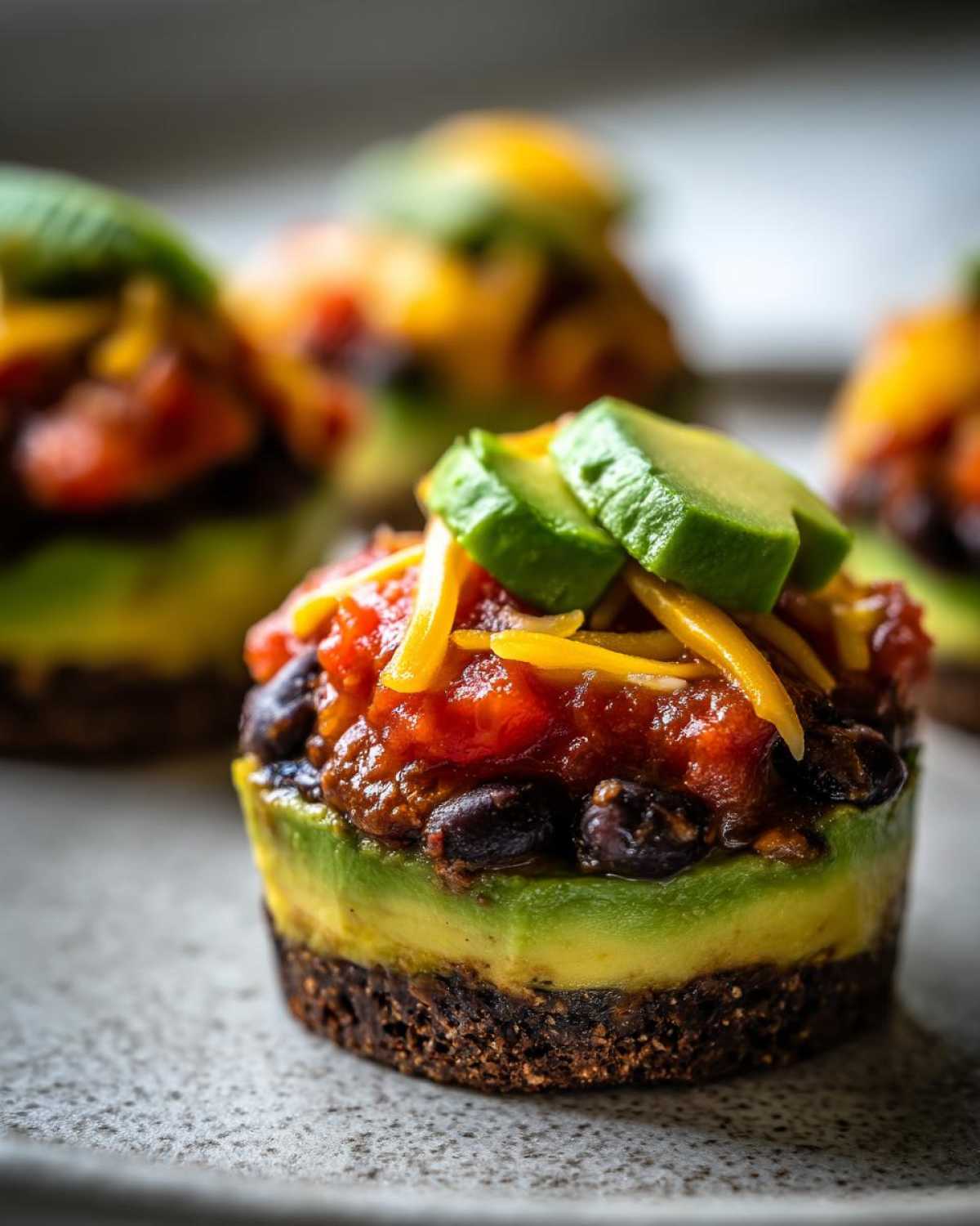 Close-up of a layered individual serving of Avocado Party Dip with a dark base, avocado layer, black beans, salsa, cheese, and fresh avocado slices.