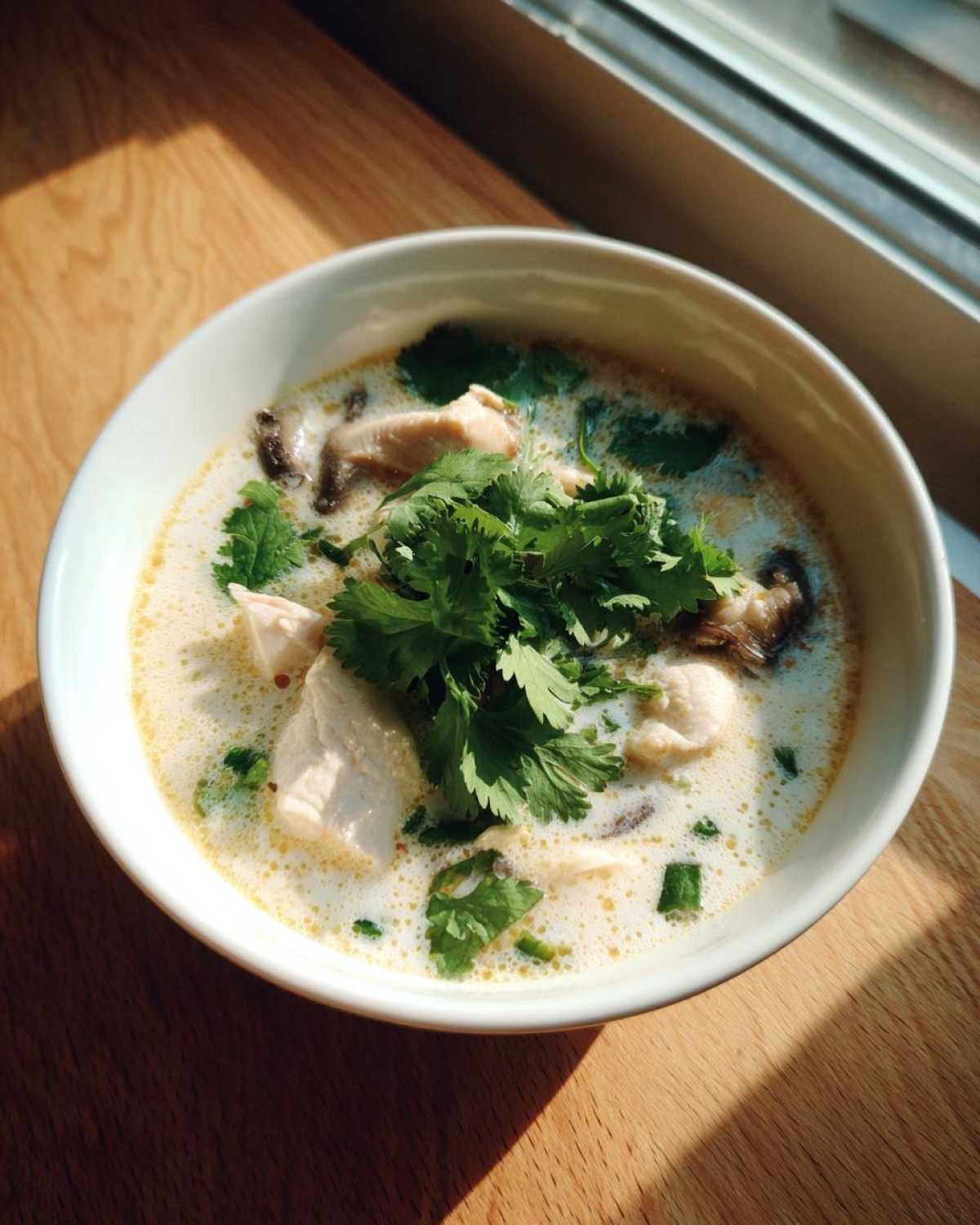 A creamy bowl of Irresistible Thai Chicken Soup topped generously with fresh cilantro and visible pieces of chicken and mushrooms.