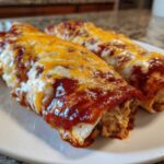 Two baked Joanna Gaines Enchiladas covered in red sauce and melted cheddar and Monterey Jack cheese.