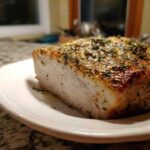 Cross-section of a perfectly cooked, juicy baked chicken breast seasoned heavily with herbs.