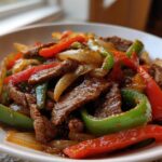 Close-up of a white bowl filled with glossy Keto Beef Pepper Steak mixed with vibrant green and red bell peppers and onions.