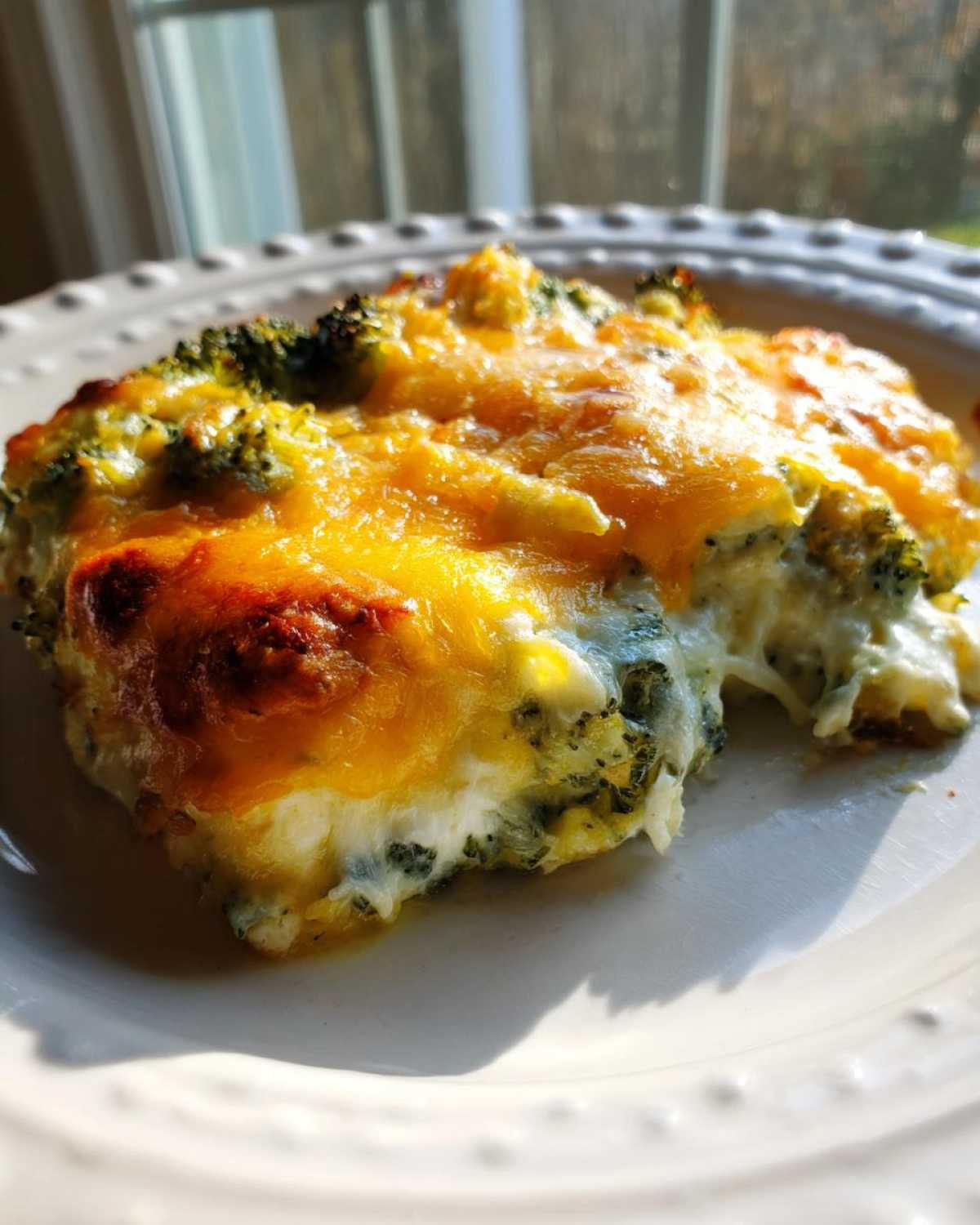 A close-up of a serving of Keto Broccoli Au Gratin, featuring creamy sauce and a bubbly, golden-brown melted cheddar cheese topping.