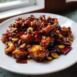 Close-up of glossy, saucy Keto Kung Pao Chicken pieces garnished with dried red chilies and peanuts.