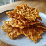 Close-up of a stack of golden-brown, crispy Keto Sour Cream Crackers seasoned with salt and pepper on a speckled grey plate.