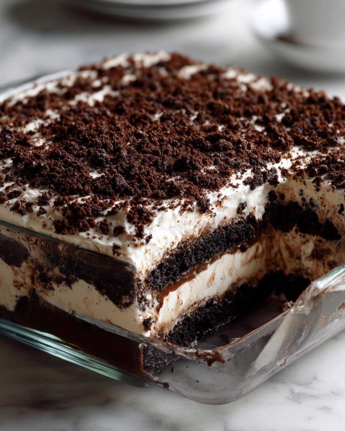 A slice removed from a glass dish revealing the layers of creamy filling and chocolate cookie crumbs in this amazing dirt cake.