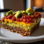 Close-up of a square serving of layered Avocado Party Dip showing layers of bean base, guacamole, cheese, salsa, and diced avocado.