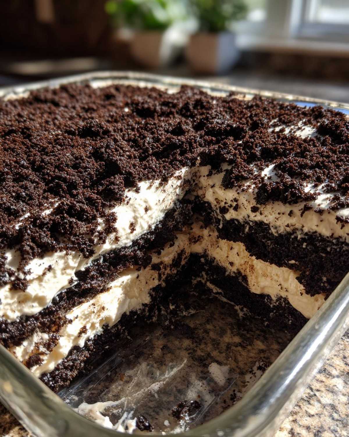 A square glass dish showing a serving removed from the layered dirt cake, revealing alternating layers of cream filling and crushed chocolate cookies.