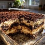 Close-up of a rich, layered dirt cake with cream filling and crushed cookie topping in a glass baking dish.