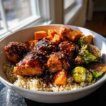 A close-up of a Maple Dijon Chicken Bowl featuring glazed chicken pieces, roasted sweet potatoes, Brussels sprouts, and quinoa.