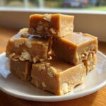 A stack of rich, brown maple fudge squares studded with chopped nuts, sitting on a white plate.