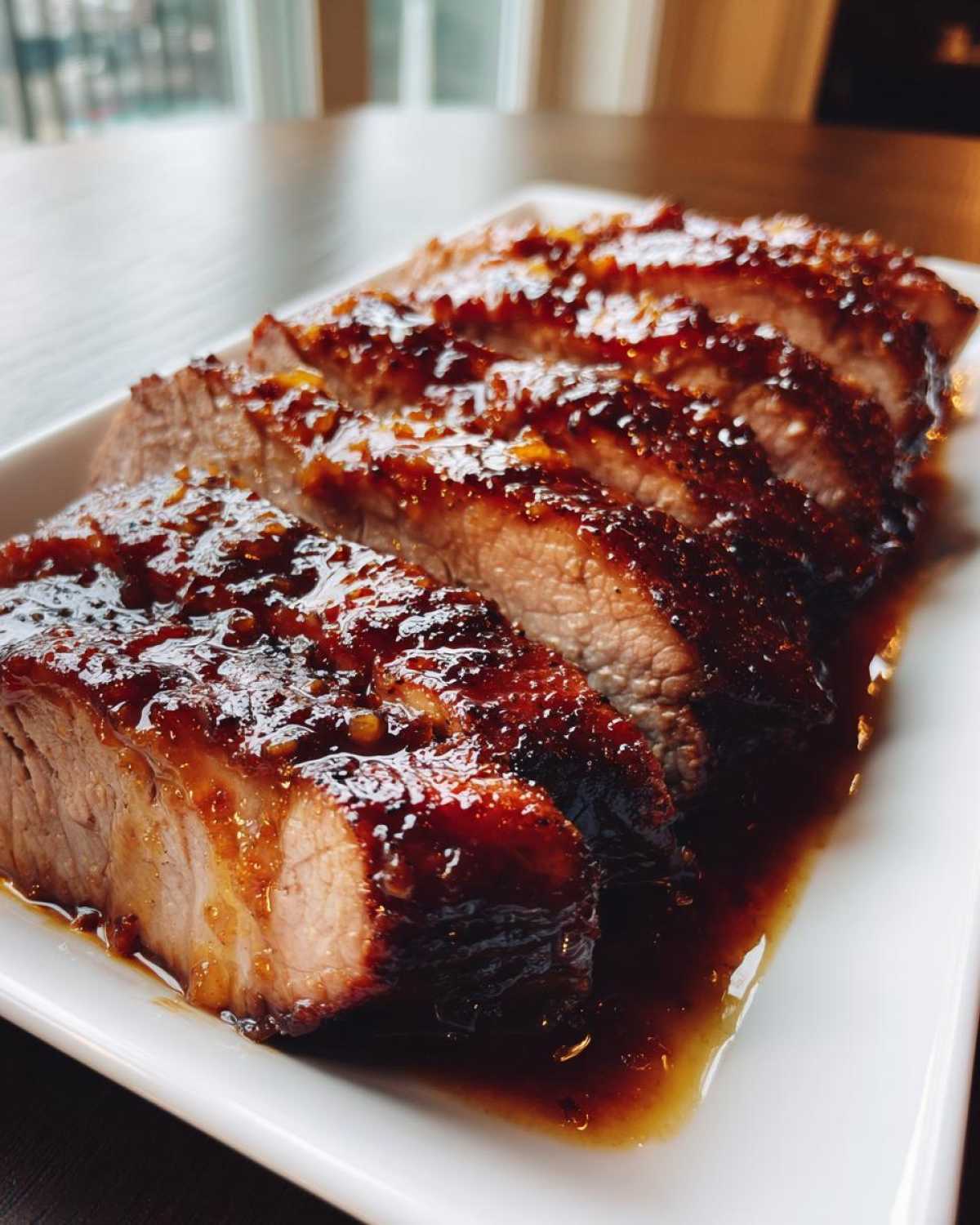 Slices of juicy maple mustard pork tenderloin covered in a thick, dark glaze served on a white platter.