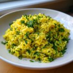 A close-up of bright yellow mediterranean rice generously topped with chopped fresh green parsley.