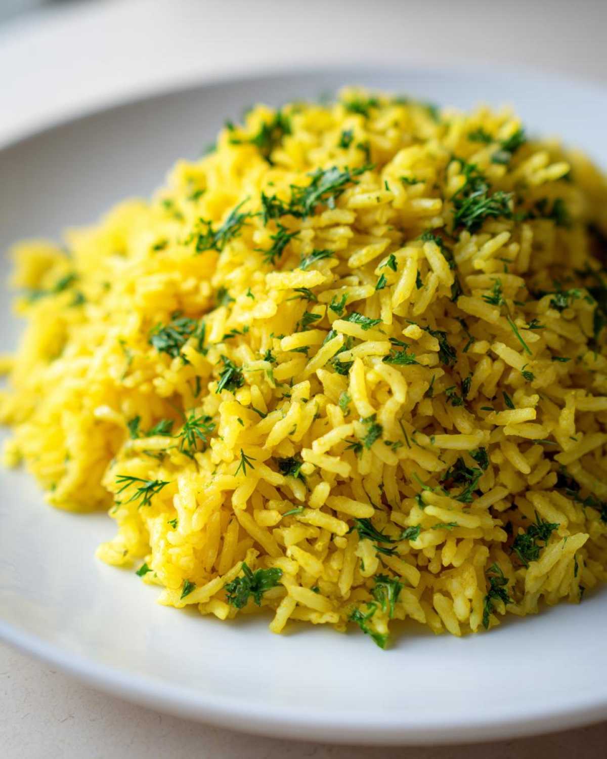 Close-up of fluffy, yellow mediterranean rice garnished with chopped fresh green herbs on a white plate.