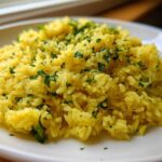 Close-up of fluffy, yellow mediterranean rice topped generously with chopped fresh parsley on a white plate.