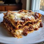 A generous, layered slice of Million Dollar Italian Lasagna featuring rich meat sauce and melted cheese on a white plate.