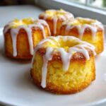 Close-up of four moist Mini Lemon Cakes Recipe bites topped with dripping white glaze and lemon zest.