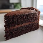 A close-up of a perfectly moist slice of two-layer chocolate cake with thick chocolate frosting.