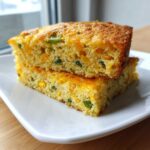 Two moist slices of mexican cornbread stacked, showing corn kernels and green chilies inside.