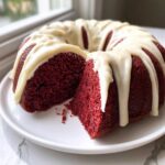 A slice cut from a vibrant red velvet bundt cake topped with thick white cream cheese glaze drips.