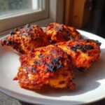 Four pieces of intensely red, charred Nando's Peri Peri Chicken Copycat resting on a white plate.