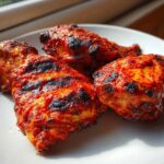 Close-up of three pieces of spicy, grilled Nando's Peri Peri Chicken Copycat on a white plate.