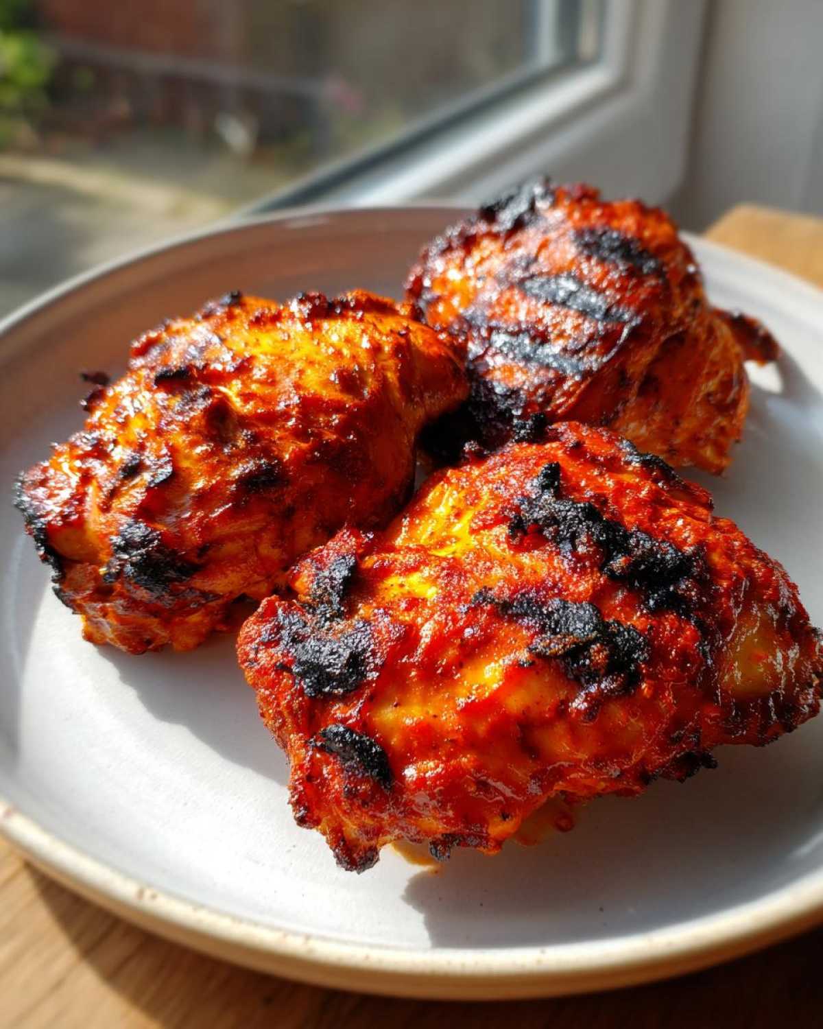 Three pieces of vibrant, charred Nando's Peri Peri Chicken Copycat thighs resting on a light grey plate.
