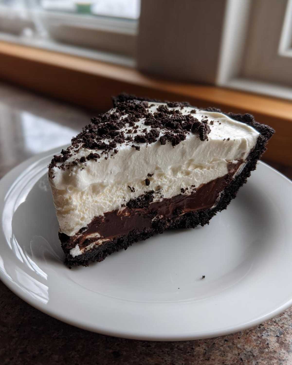 A perfect slice of no bake Oreo pie showing a dark chocolate filling and white whipped topping, sprinkled with cookie crumbs.