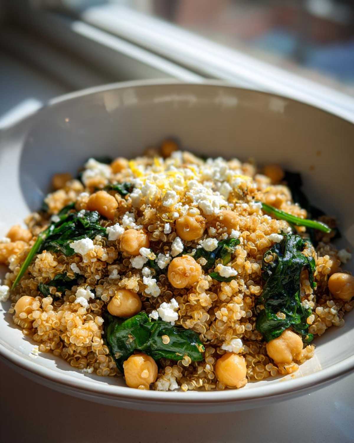 A close-up bowl of One Pot Chickpea Quinoa Recipe mixed with spinach and topped with feta cheese.
