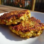 Close-up of two golden-brown Oven-Baked Cabbage Burgers stacked slightly on a white plate outdoors.