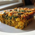 A close-up, sunlit slice of baked Quinoa Lentil Spinach Casserole showing visible quinoa grains and dark green spinach.