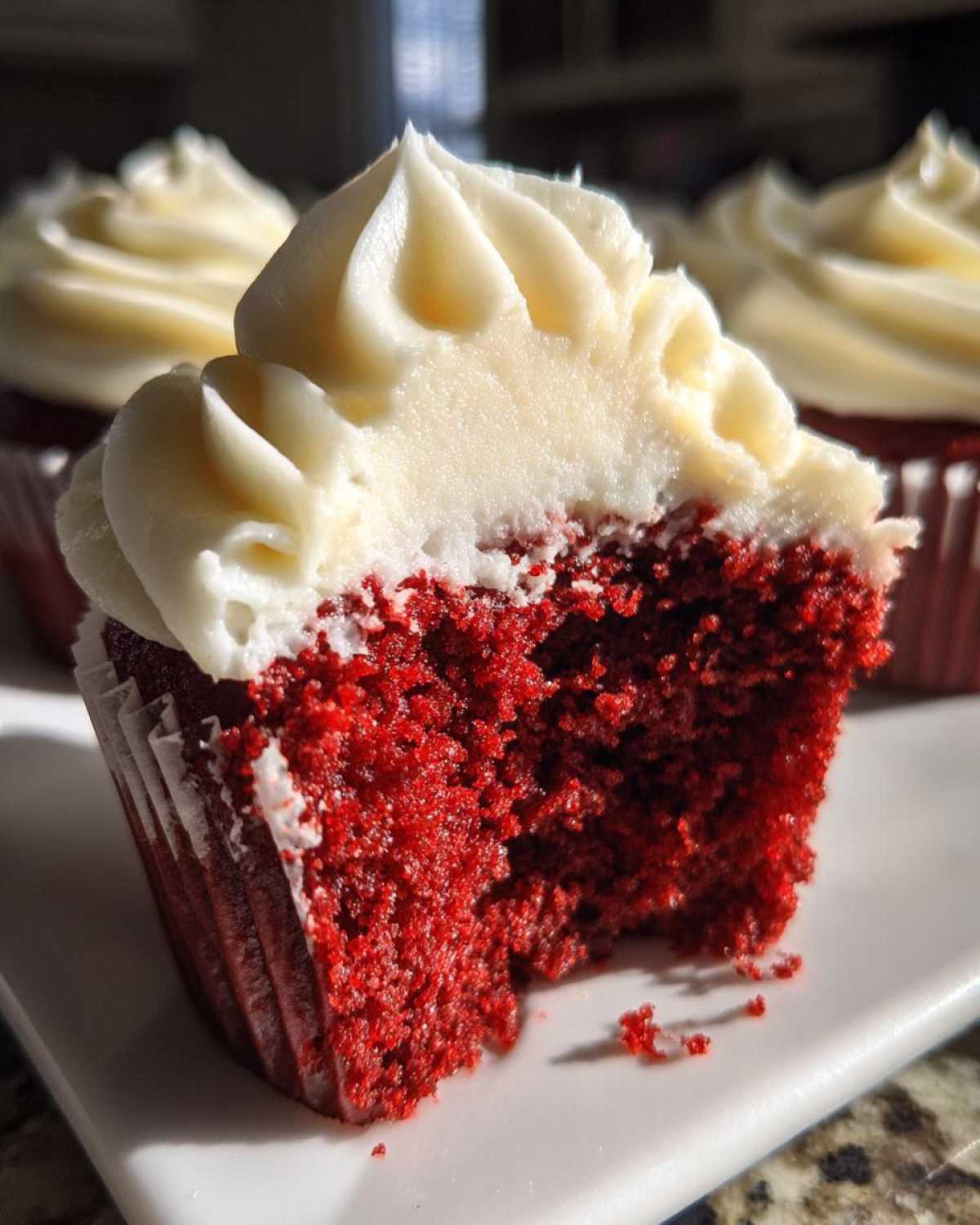 A close-up of a red velvet cupcakes cut in half showing the vibrant red crumb and thick cream cheese frosting.