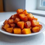 A mound of beautifully caramelized roasted butternut squash cubes piled high on a white plate.
