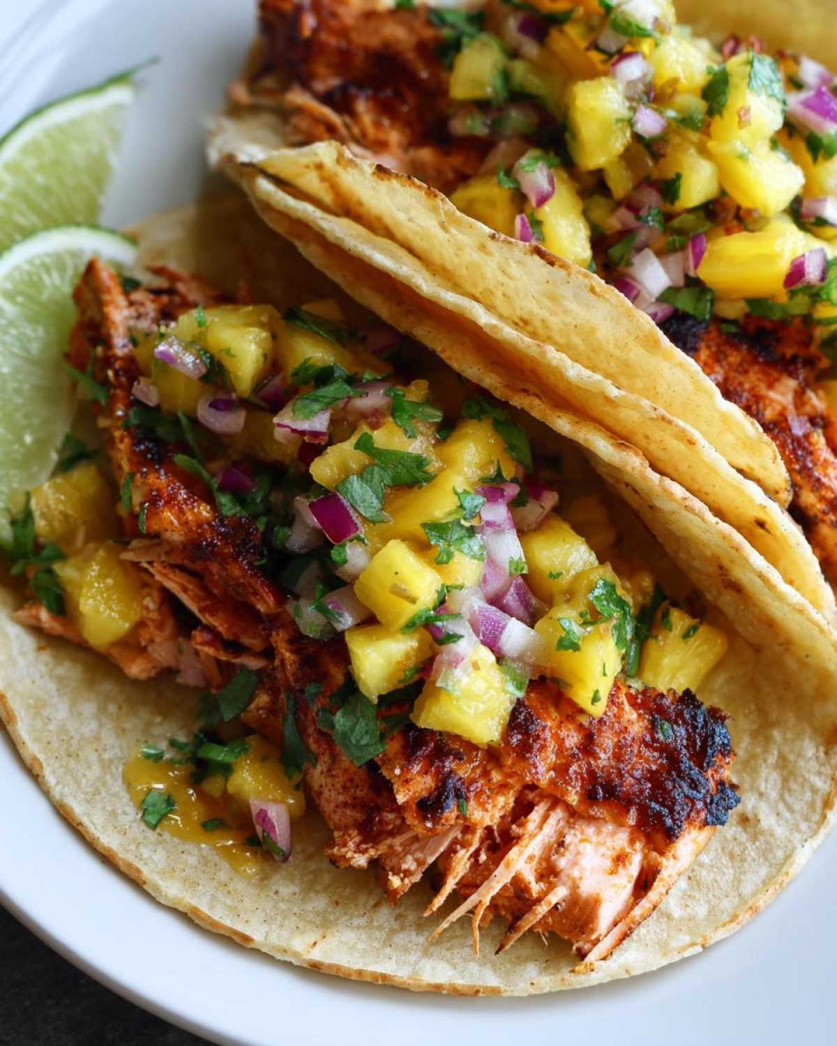 Two delicious Salmon Tacos topped generously with vibrant pineapple salsa and served with lime wedges.