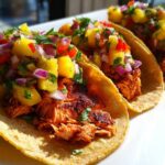Three delicious Salmon Tacos with Pineapple Salsa piled high on soft corn tortillas, served on a white plate.
