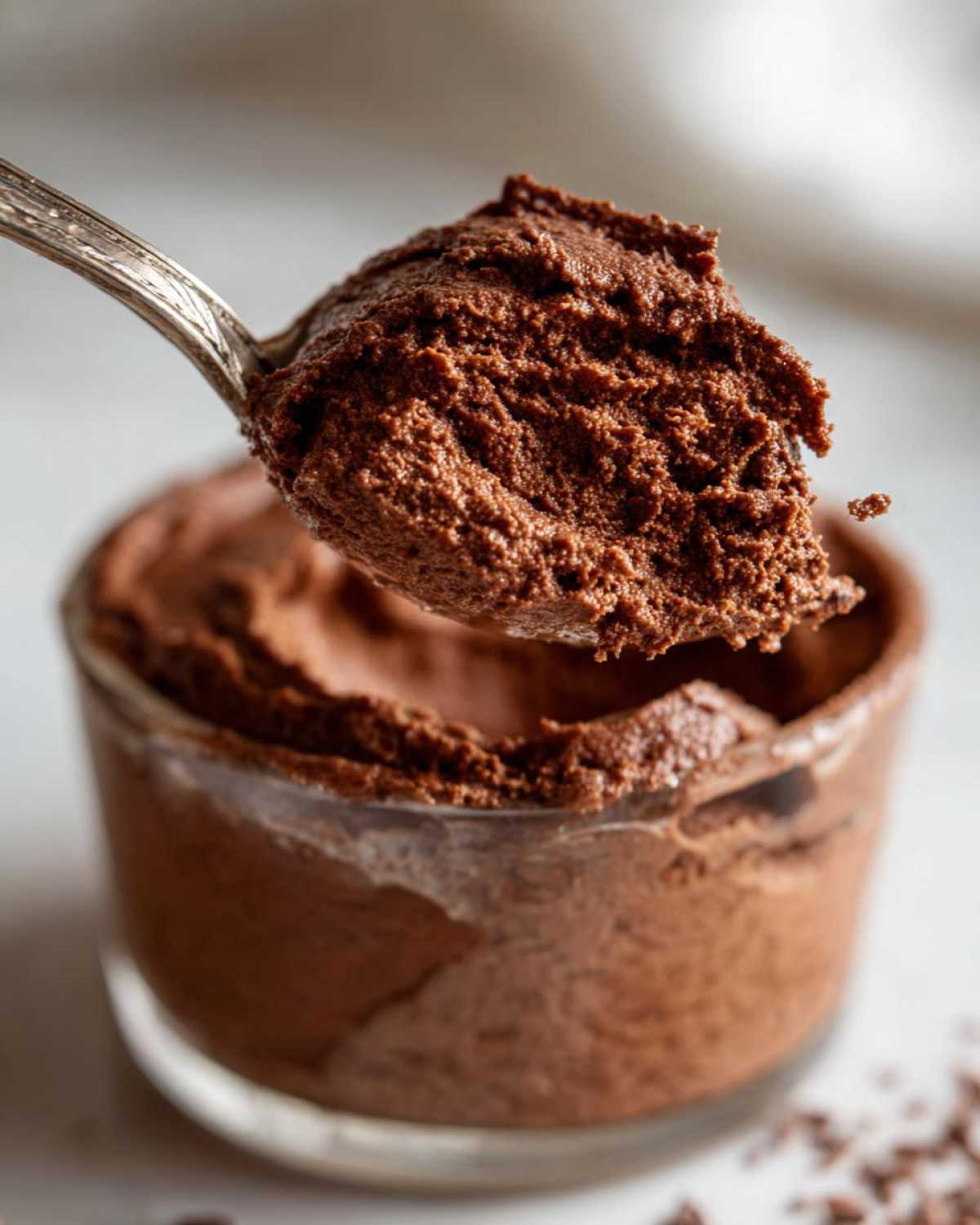 Close-up of a spoonful of airy, dark chocolate mousse being lifted from a glass serving dish.
