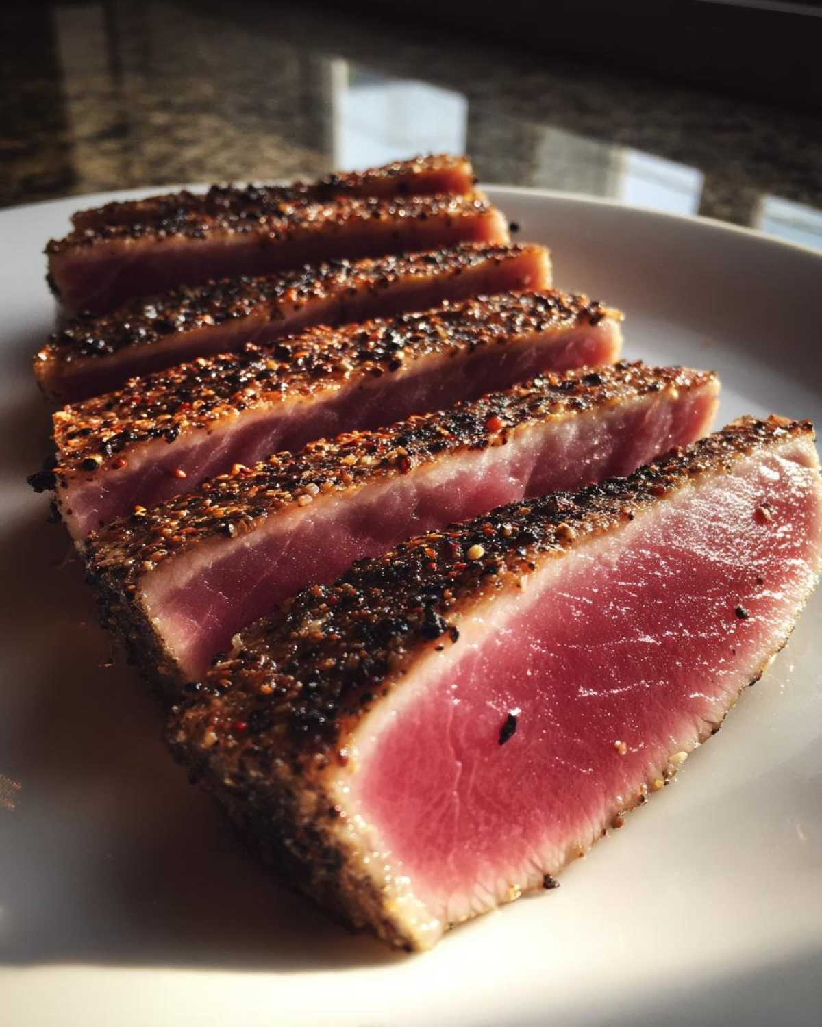 Close-up of perfectly seared, pepper-crusted Tuna Steaks, sliced to show the rare, pink center.