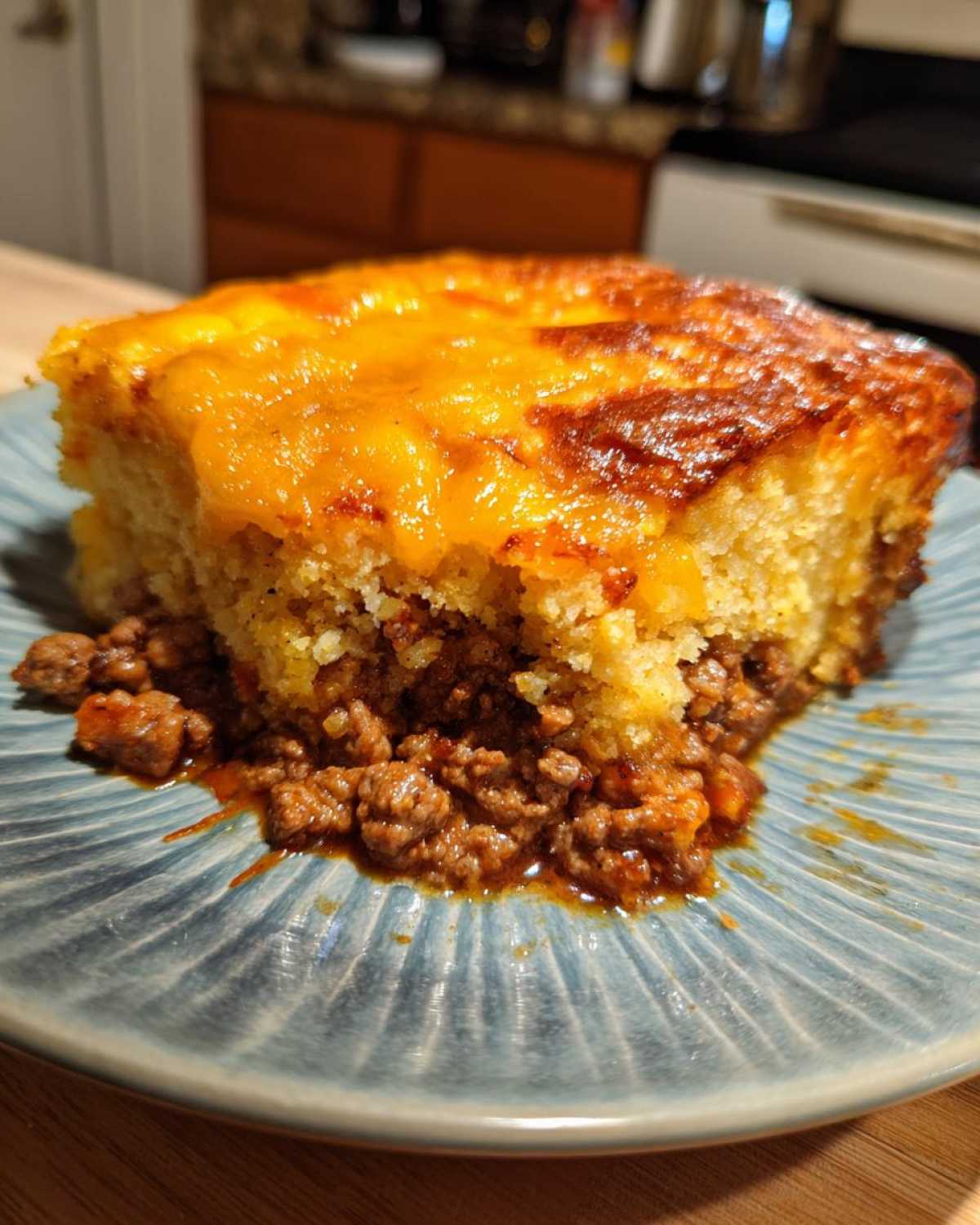 A close-up serving of tamale pie showing a layer of seasoned ground meat topped with thick cornbread and melted cheddar cheese.