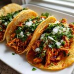 Three crispy corn shell chicken tacos filled with shredded seasoned chicken, topped with fresh diced white onion and cilantro.