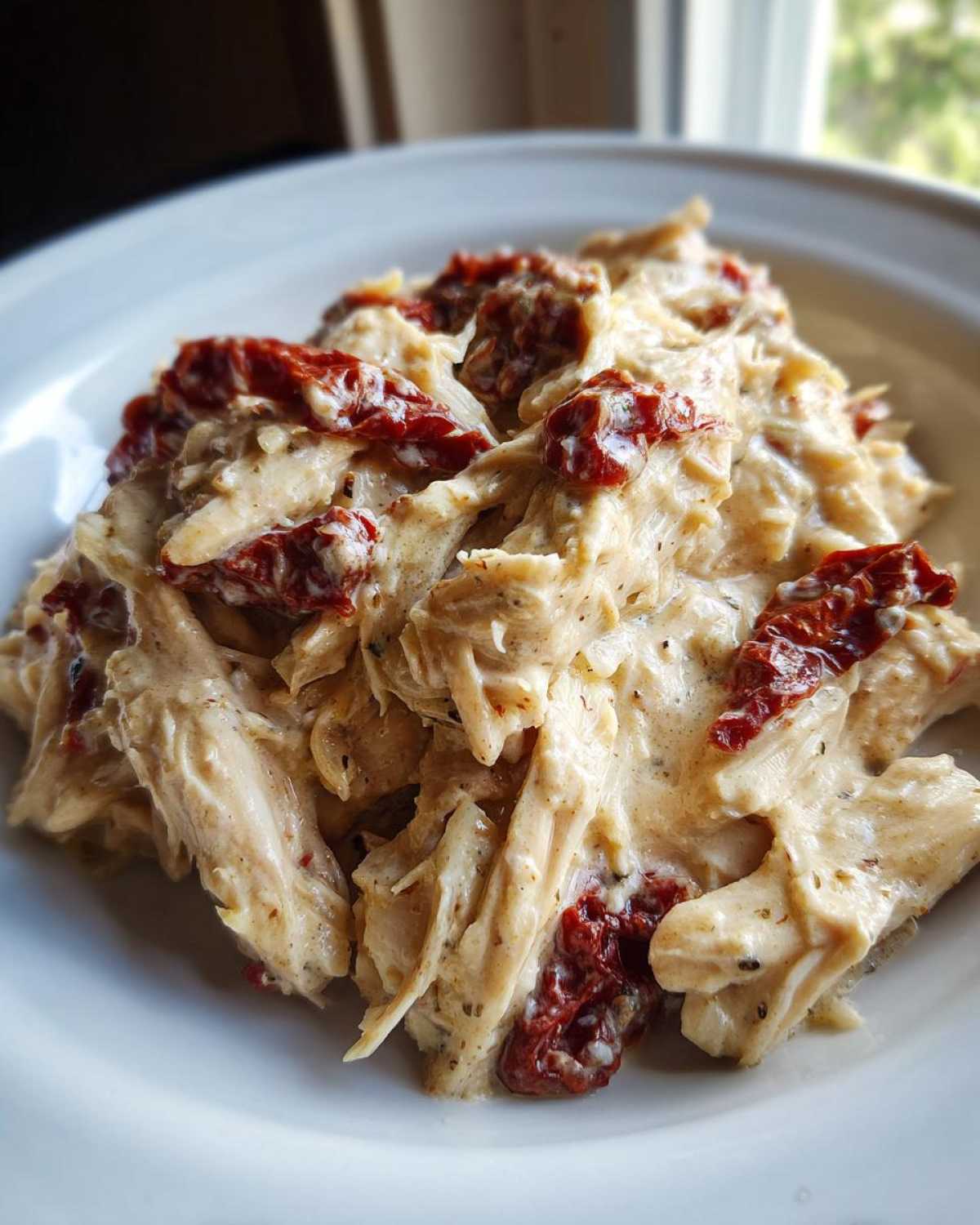 Close-up of shredded crockpot marry me chicken coated in a creamy sauce with visible pieces of sun-dried tomatoes.