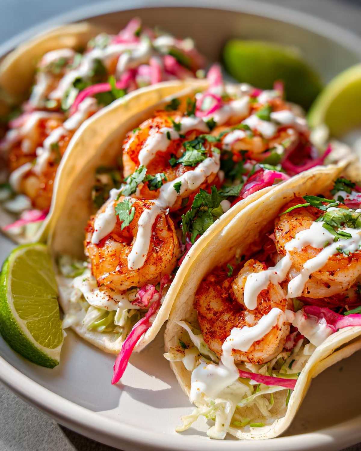 Three delicious Shrimp Tacos with Lime Crema, seasoned shrimp, slaw, and cilantro on soft tortillas.