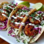 Three delicious Shrimp Tacos with lime crema drizzle, seasoned shrimp, and purple cabbage slaw.
